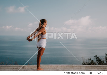 Fitness woman sea. A happy middle aged woman in white sportswear exercises morning outdoors in a park with a beach view. Female fitness pilates yoga routine concept. Healthy lifestyle. 101065233