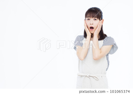 A housewife in her thirties in an apron who is surprised in front of a white background 101065374