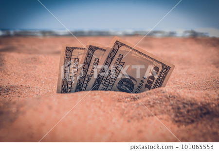 Money dolars half covered with sand lie on sandy beach near sea ocean waves on sunny summer day close-up. Money grows out of the ground. Concept finance money holiday relax vacation. Money dolars half covered with sand lie on sandy beach near sea ocean waves on sunny summer day close-up. Money grows out of the ground. Concept finance money holiday relax vacation. 101065553
