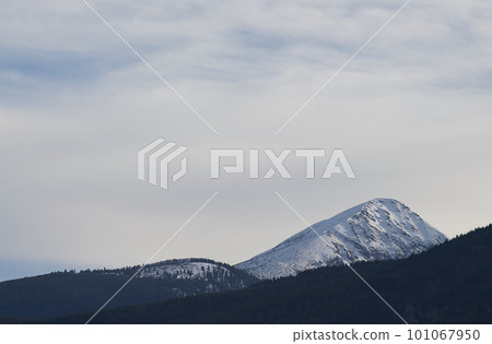 Snowy mountain peak in daylight with bright sky and shadowed slope. 101067950