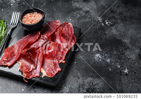 Turkish sliced pastrami (kayseri pastirma), dried beef meat with spices on marble board. Black background. Top view. Copy space Turkish sliced pastrami (kayseri pastirma), dried beef meat with spices on marble board. Black background. Top view. Copy space 101069235