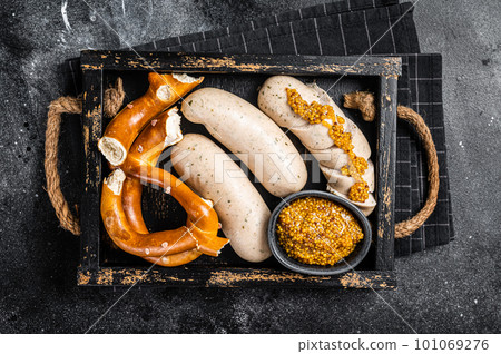 Bavarian meal with white sausages and sweet mustard in wooden tray with Pretzel. Black background. Top view Bavarian meal with white sausages and sweet mustard in wooden tray with Pretzel. Black background. Top view 101069276