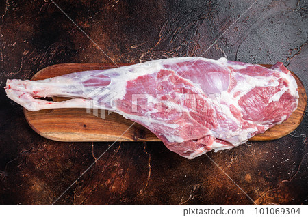 Raw whole lamb leg thigh on butcher board. Dark background. Top view 101069304