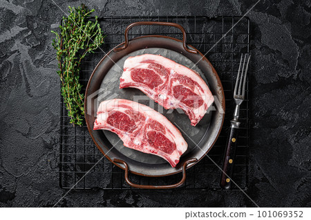 Raw fresh lamb loin chops with herbs and spices in steel tray. Black background. Top view 101069352