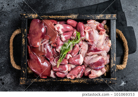 Uncooked Bird offals, raw chicken giblets, gizzards, stomachs, liver and hearts in a wooden tray. Black background. Top view 101069353