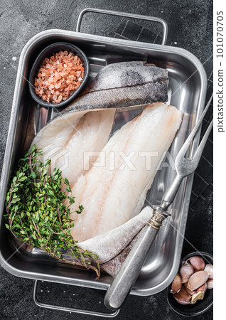 Raw haddock fish fillets, whitefish meat in kitchen tray with thyme. Black background. Top view Raw haddock fish fillets, whitefish meat in kitchen tray with thyme. Black background. Top view 101070705