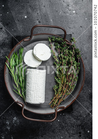 Chevre goat soft cheese with herbs on a tray. Black background. Top view Chevre goat soft cheese with herbs on a tray. Black background. Top view 101070742