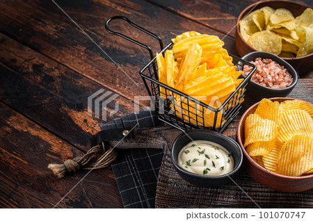 Mix of Crinkle Potato chips served with dip sauce and sea salt. Wooden background. Top view. Copy space Mix of Crinkle Potato chips served with dip sauce and sea salt. Wooden background. Top view. Copy space 101070747
