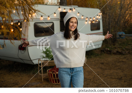 A pensive Caucasian woman in a white knitted sweater and a hat is resting near a motorhome in a warm autumn. Travel by camper. A pensive Caucasian woman in a white knitted sweater and a hat is resting near a motorhome in a warm autumn. Travel by camper. 101070786