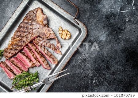 Medium rare Grilled T-Bone Steak, Florentine steak sliced in a steel tray. Black background. Top view. Copy space 101070789