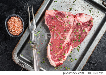 T-bone steak, raw marbled beef meat in a steel kitchen tray with herbs. Black background. Top view T-bone steak, raw marbled beef meat in a steel kitchen tray with herbs. Black background. Top view 101070794