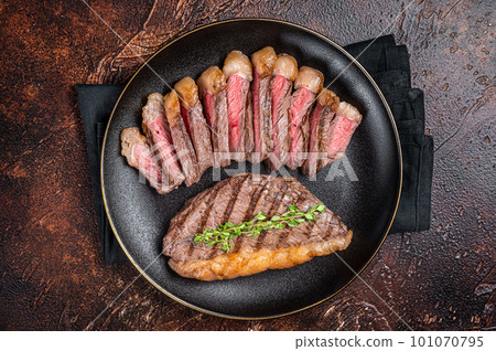 Sliced grilled medium rare Top sirloin beef steak on a plate. Dark background. Top view 101070795