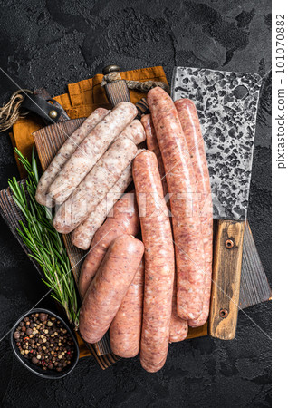 Mix fresh raw sausages. Beef, pork, lamb and chicken mince meat sausages on a butcher cutting board with spices. Black background. Top view 101070882