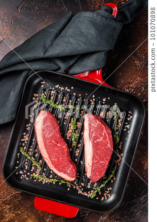 Sirloin steak or brazilian Picanha, raw marbled beef meat with on a grill skillet. Dark background. Top view 101070898