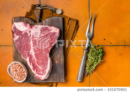 Porterhouse raw beef meat Steak, T-bone with thyme and sea salt on a wooden board. Orange background. Top view 101070901