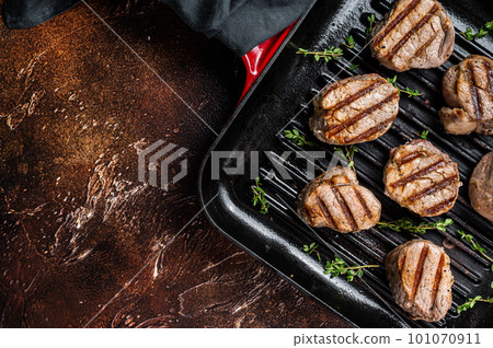 Fried pork medallions steaks from tenderloin meat on a grill skillet. Dark background. Top view. Copy space Fried pork medallions steaks from tenderloin meat on a grill skillet. Dark background. Top view. Copy space 101070911