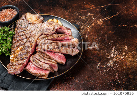Grilled Medium rare Porterhouse, T-Bone Steak sliced in a plate. Dark background. Top view. Copy space 101070936