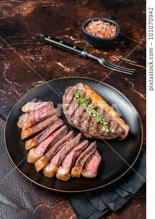 Sliced grilled medium rare Top sirloin beef steak on a plate. Dark background. Top view 101070942