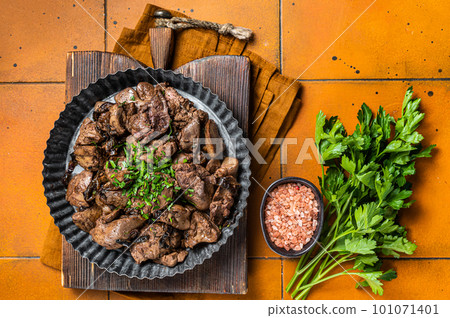 Roast chicken liver with onions and herb in a steel plate. Orange background. Top view 101071401