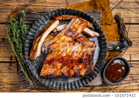 Smoked pork spare ribs glazed in BBQ sauce in a steel plate. Wooden background. Top view Smoked pork spare ribs glazed in BBQ sauce in a steel plate. Wooden background. Top view 101071432