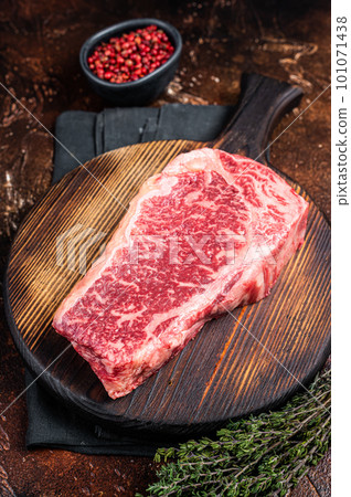 Uncooked Raw striploin or club steak on wooden board with thyme. Dark background. Top view 101071438