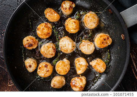 Fried scallops with butter lemon sauce in a skillet. Dark background. Top view 101071455