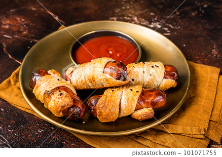Rolled hot dog sausages baked in puff pastry with ketchup. Dark background. Top view 101071755