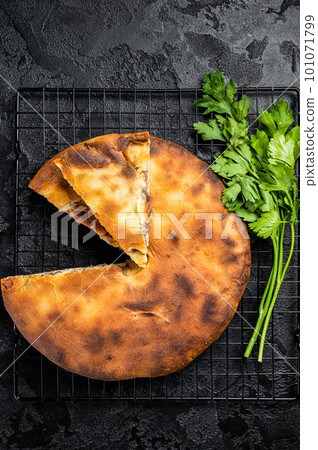 Baked Ossetian pie with beef meat and herbs. Black background. Top view Baked Ossetian pie with beef meat and herbs. Black background. Top view 101071799