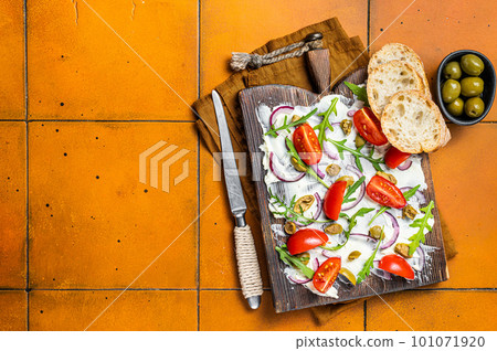 Trendy Butter Board with olives, onion, arugula, capers and tomato, Butterboard. Orange background. Top view. Copy space 101071920