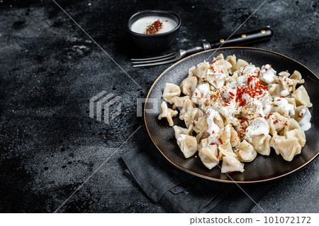 Turkish manti with yoghurt and tomato sauce in a plate. Black background. Top view. Copy space 101072172