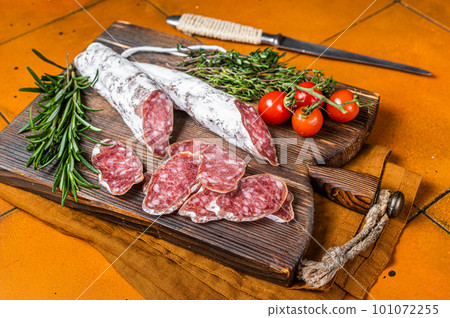 Spanish Fuet sausage slices on wooden cutting board. Orange background. Top view Spanish Fuet sausage slices on wooden cutting board. Orange background. Top view 101072255