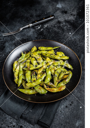 Stir-fried green Edamame Soy Beans with sea salt and sesame seeds in a plate. Black background. Top view 101072361