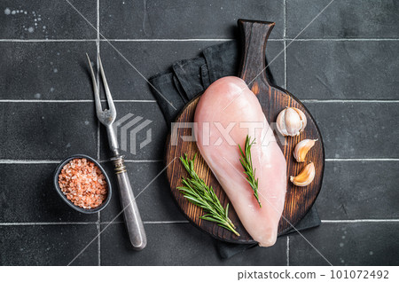 Raw chicken breast fillet on a wooden board with rosemary and garlic, poultry meat. Black background. Top view Raw chicken breast fillet on a wooden board with rosemary and garlic, poultry meat. Black background. Top view 101072492