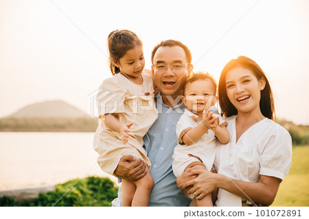 A happy group of children and parents laughing and having fun together in a park, joyful family of four enjoying the warmth of the sunshine and the beauty of the outdoors, Family Day 101072891