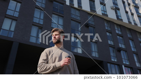 Attractive bearded man holding take away cup with coffee office center on background. 101073066