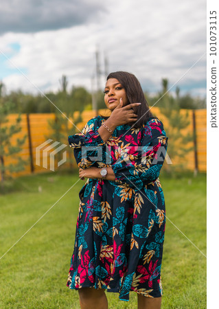 Summer portrait of beautiful african american woman in colourful dress wear standing on backyard. Suburban lifestyle and chilling on weekend in countryside and inclusion with diversity concept 101073115