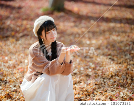 A young woman picking up autumn leaves in a park full of sunshine filtering through foliage A young woman picking up autumn leaves in a park full of sunshine filtering through foliage 101073181