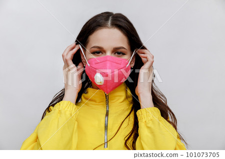 Young brunette woman wants to put on a pink ffp2 protective mask on whote background. 101073705