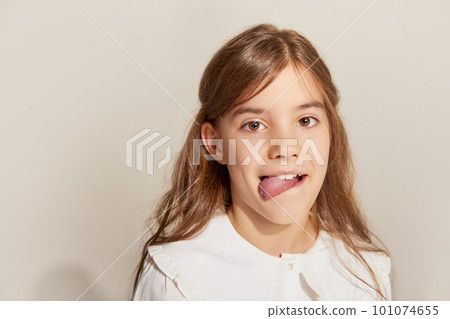 Close up portrait of one little charming girl with long hair grimacing and looking at camera over light background 101074655