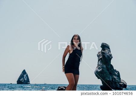 Woman summer travel sea. Happy tourist in hat enjoy taking picture outdoors for memories. Woman traveler posing on the beach at sea surrounded by volcanic mountains, sharing travel adventure journey Woman summer travel sea. Happy tourist in hat enjoy taking picture outdoors for memories. Woman traveler posing on the beach at sea surrounded by volcanic mountains, sharing travel adventure journey 101074656
