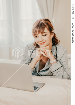 Freelancer woman wears pajamas, she lies in bed and uses work on 101074841