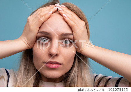 close-up of a sad girl in casual clothes holding her head on a blue isolated background close-up of a sad girl in casual clothes holding her head on a blue isolated background 101075155