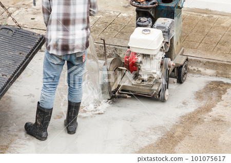 Worker using diamond saw blade machine cutting concrete road at construction site 101075617
