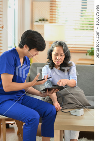 Shot of health visitor giving recommendations and measuring blood pressure middle age woman patient during home visit 101075968