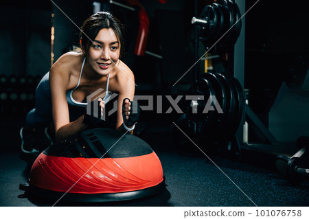 Slim Asian woman performing a plank exercise on a stability ball, demonstrating balance and agility while improving her overall body shape, exercise in dark gym background Slim Asian woman performing a plank exercise on a stability ball, demonstrating balance and agility while improving her overall body shape, exercise in dark gym background 101076758
