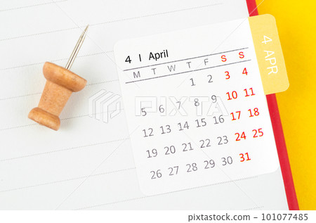 A April mini calendar on a white note book with wooden push pin on yellow background. 101077485