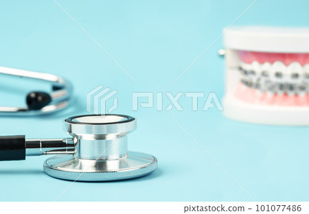 A Medicine equipment stethoscope and metal wire dental braces on model teeth on blue background. Health dental care concept. 101077486