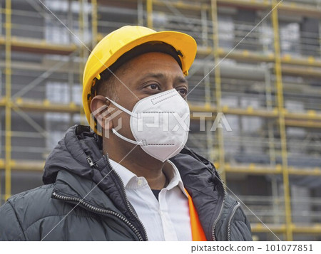 Indian construction worker wearing a safety helmet and a protective ffp2 mask posing on construction site 101077851