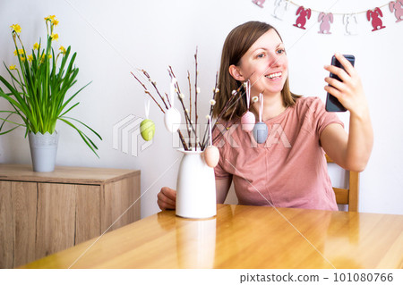 Attractive smiling woman talk on a video call using a smartphone. Young girl making on Easter selfie Attractive smiling woman talk on a video call using a smartphone. Young girl making on Easter selfie 101080766