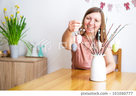 Smiling woman decorating a bouquet of willow brunches with colored Easter eggs at home. Smiling woman decorating a bouquet of willow brunches with colored Easter eggs at home. 101080777